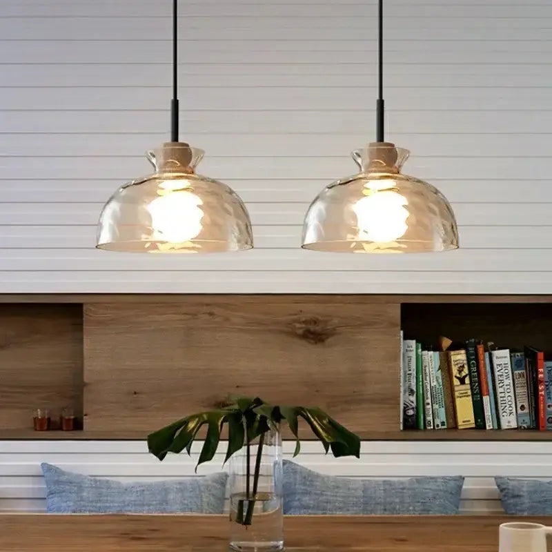 Two warm-toned decorbites clear glass pendant lamps with hammered texture hang above a wooden table