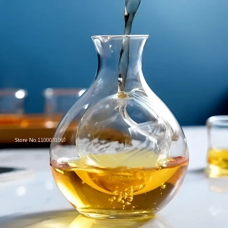 A clear crystal glass wine decanter with a bulbous body filled halfway with golden liquid for modern decorbites crystal glass use