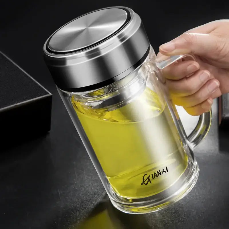 Modern insulated glass tea cup with clear double-walled glass, silver stainless steel lid and handle, filled with yellow liquid