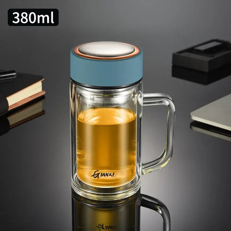 Modern insulated glass tea cup with clear double-walled glass, light blue lid and handle, filled with golden tea