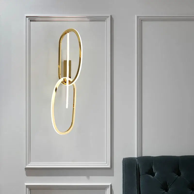 Modern interlocking oval gold wall sconce lighting fixture with two rings and central led strip for bedroom decorbites gold led