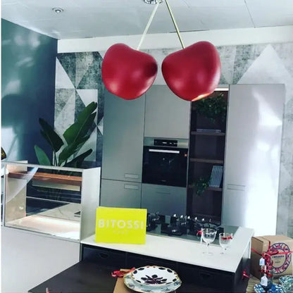 Two glossy red cherry-shaped decorbites gold pendant lights hang from the ceiling in a modern dining room setting