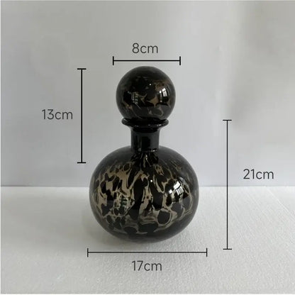 A glossy black glass perfume bottle with marbled gold and black leopard texture topped by a spherical stopper