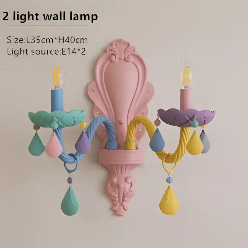 Pastel pink ornate wall sconce with two candle-style arms and teardrop crystal pendants in decorbites crystal chandelier design