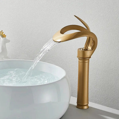 Golden waterfall basin faucet with sleek curved design flowing water into white ceramic sink for modern bathroom vanity
