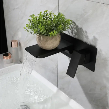 Modern matte black basin faucet with solid brass brushed gold accents and integrated shelf holding green foliage pot