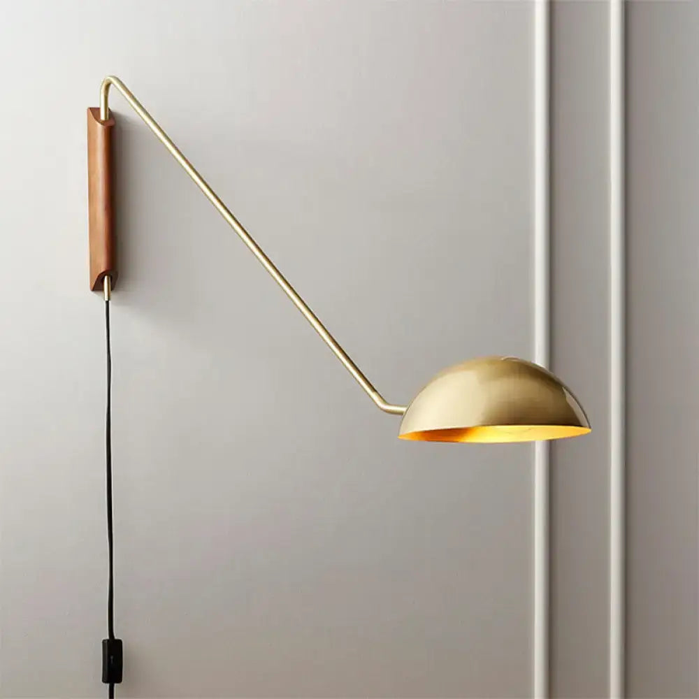 Modern gold-toned wall lamp with curved brass swing arm and wooden backplate dome shade for bedside use