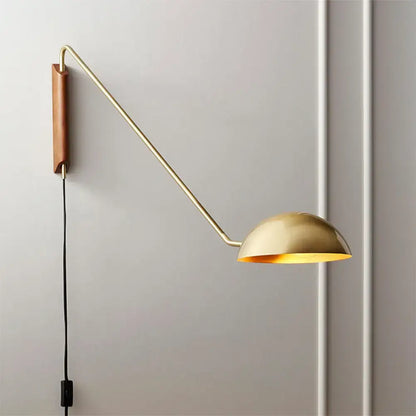 Modern gold-toned wall lamp with curved brass swing arm and wooden backplate dome shade for bedside use