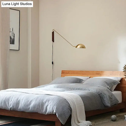 Gold-toned wall lamp with slender swing arm and dark wood bedside wall lamp base for modern bedroom use