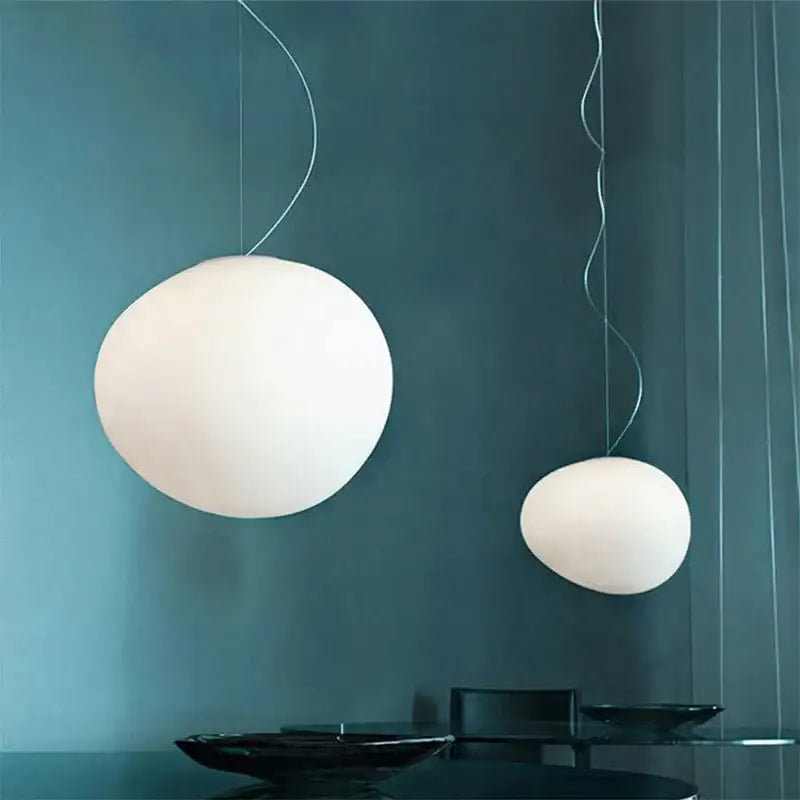 Two white matte glass gregg glass pendant lights with thin metallic cords hang against a dark teal wall for kitchen decorbites gregg glass pendant