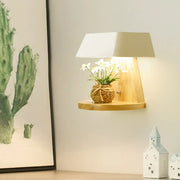 Modern metal trapezoid wall sconce with wooden backplate light fixture featuring a white shade and shelf with flowers
