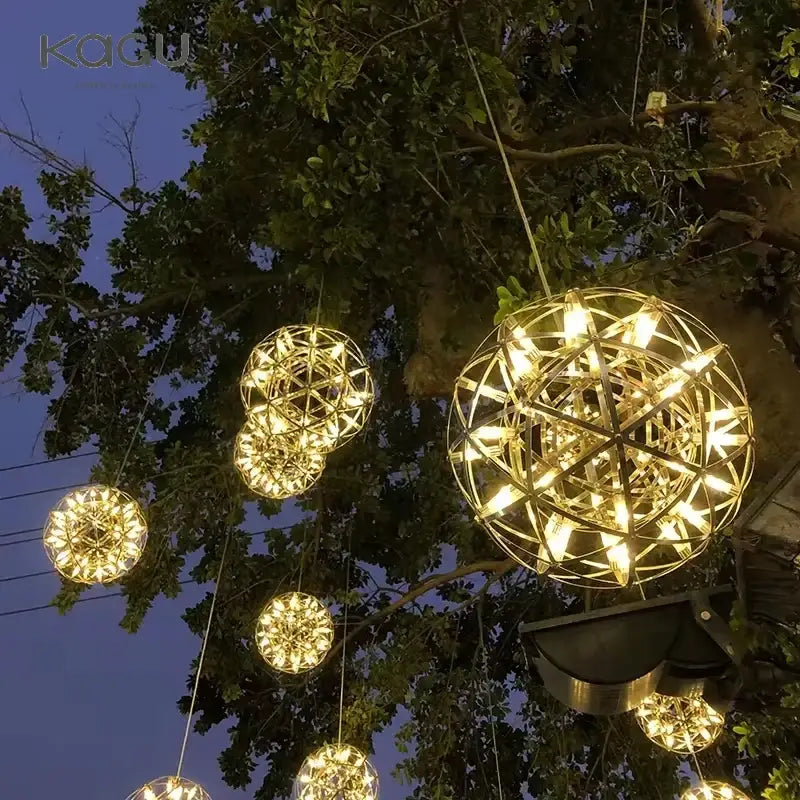 Golden spherical fireworks pendant light with intricate geometric wireframe design hanging from tree branches