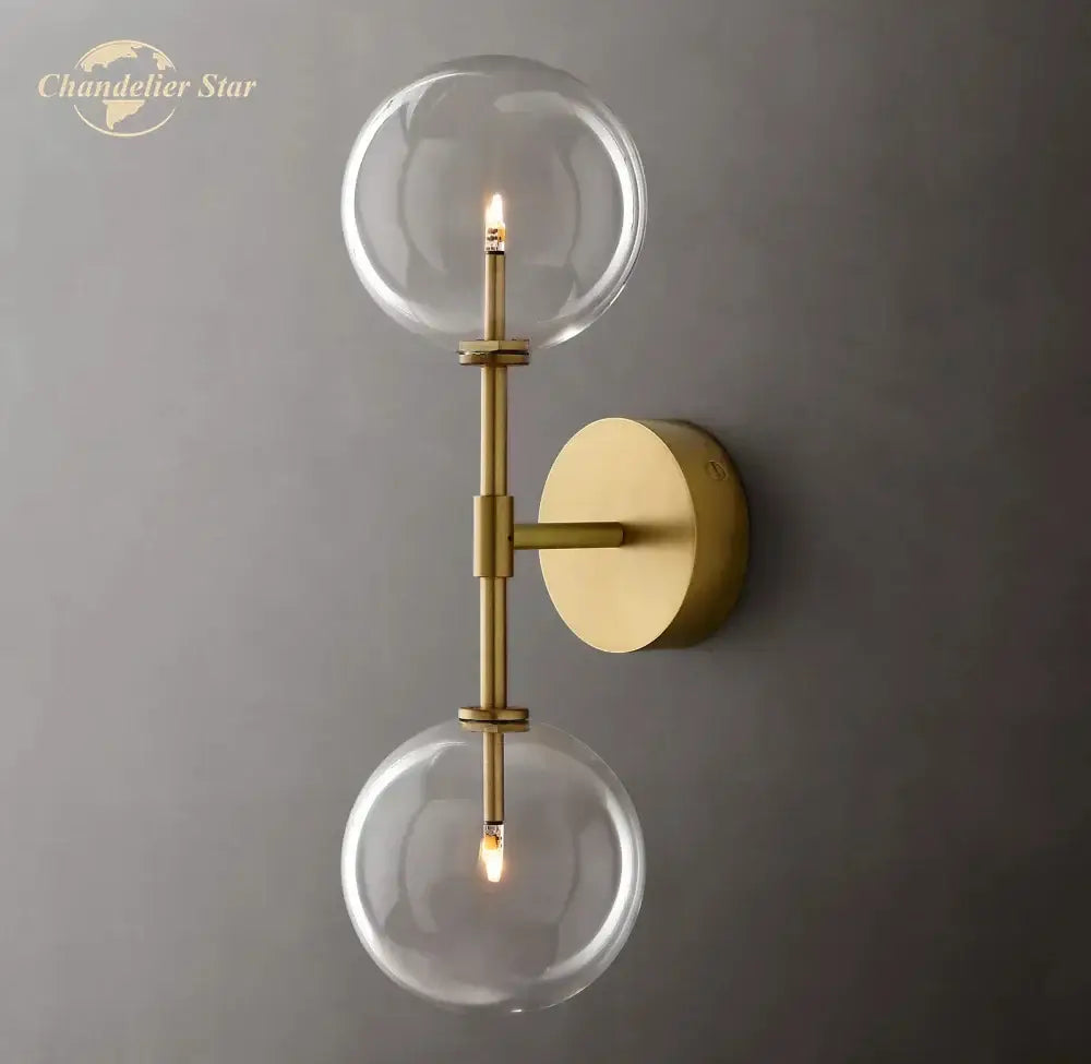 Brass-finished wall sconce with two clear glass globe shades for modern bedroom lighting using clear glass globes