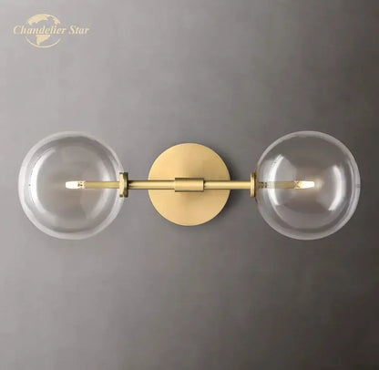Modern metallic gold-toned wall sconce with two clear glass globe shades featuring a minimalist design for bedroom lighting