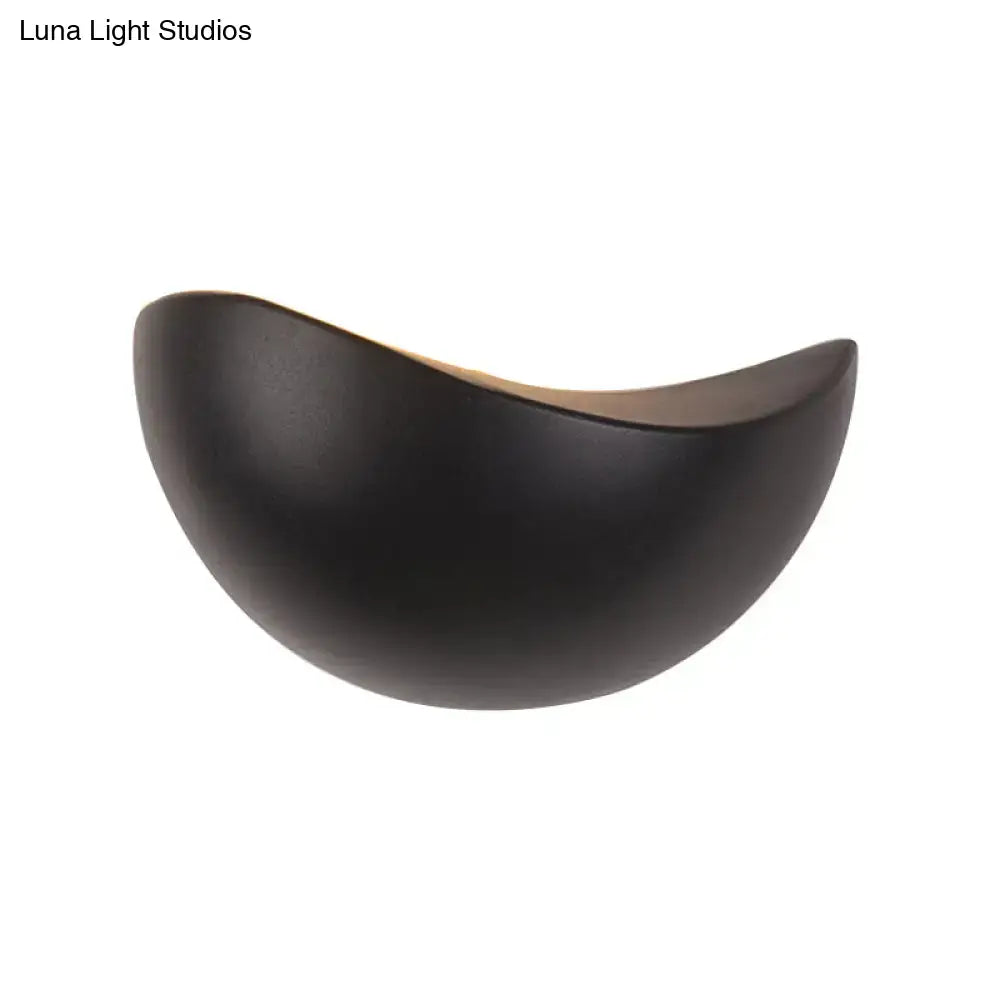 Black ceramic wall sconce with smooth curved crescent shape and warm interior for modern metallic wall washer light