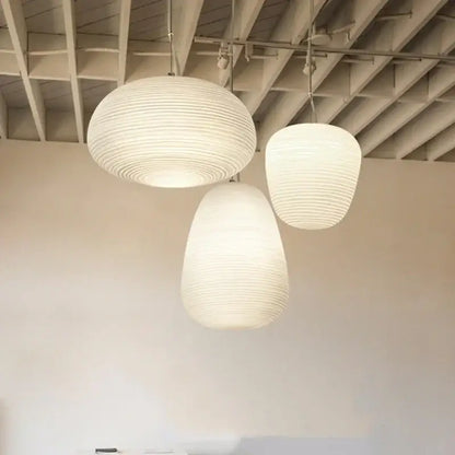 Three off-white ribbed paper lanterns hang as a modern milky white glass whorls cocoon pendant light in a dining room