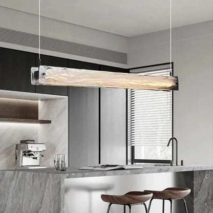 A modern minimalist cloud fog glass pendant light with textured translucent body and metallic ends above kitchen counter