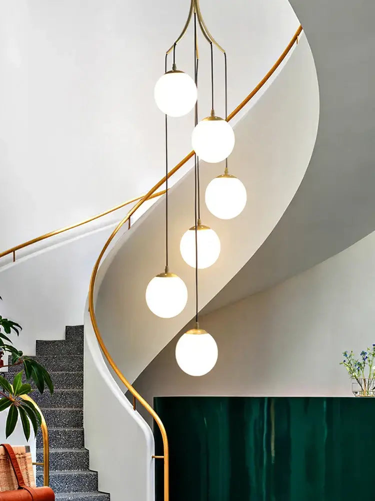 A modern brass decorbites glass ball pendant light with five frosted globes hanging vertically for staircase lighting
