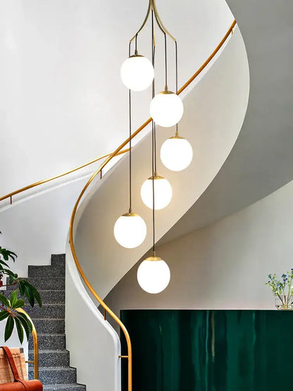 A modern brass decorbites glass ball pendant light with five frosted globes hanging vertically for staircase lighting