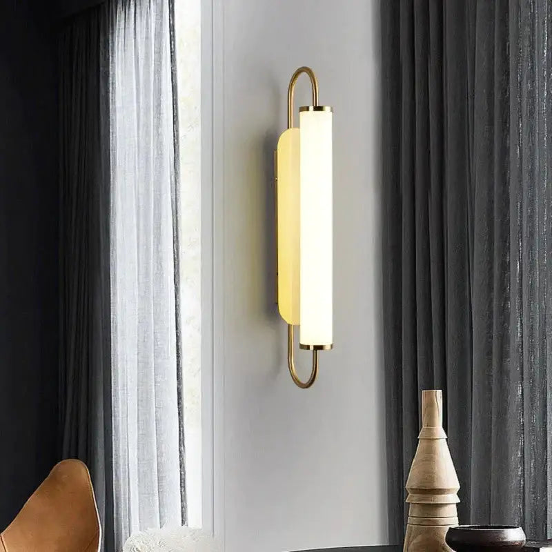 Gold-toned minimalist led wall lamp with frosted glass cylinder and curved metal frame for modern bedroom lighting