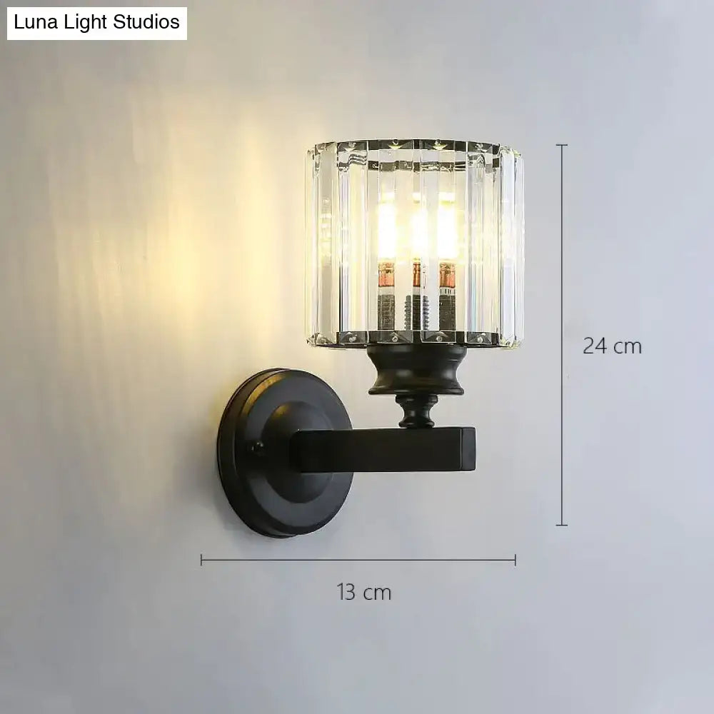 Modern minimalist black wrought iron wall sconce with cylindrical crystal glass shade for bedroom lighting