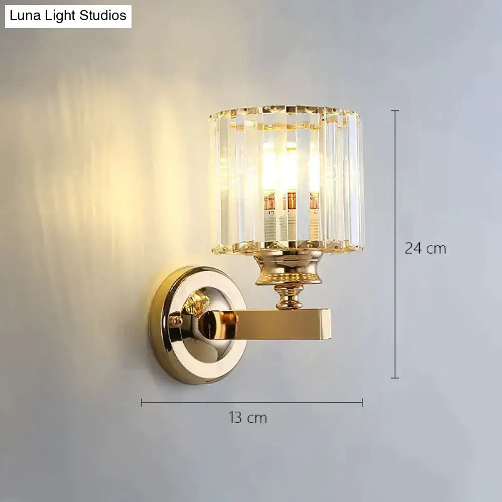 Modern minimalist wall lamp with gold-toned polished brass finish and cylindrical crystal shade for bedroom lighting