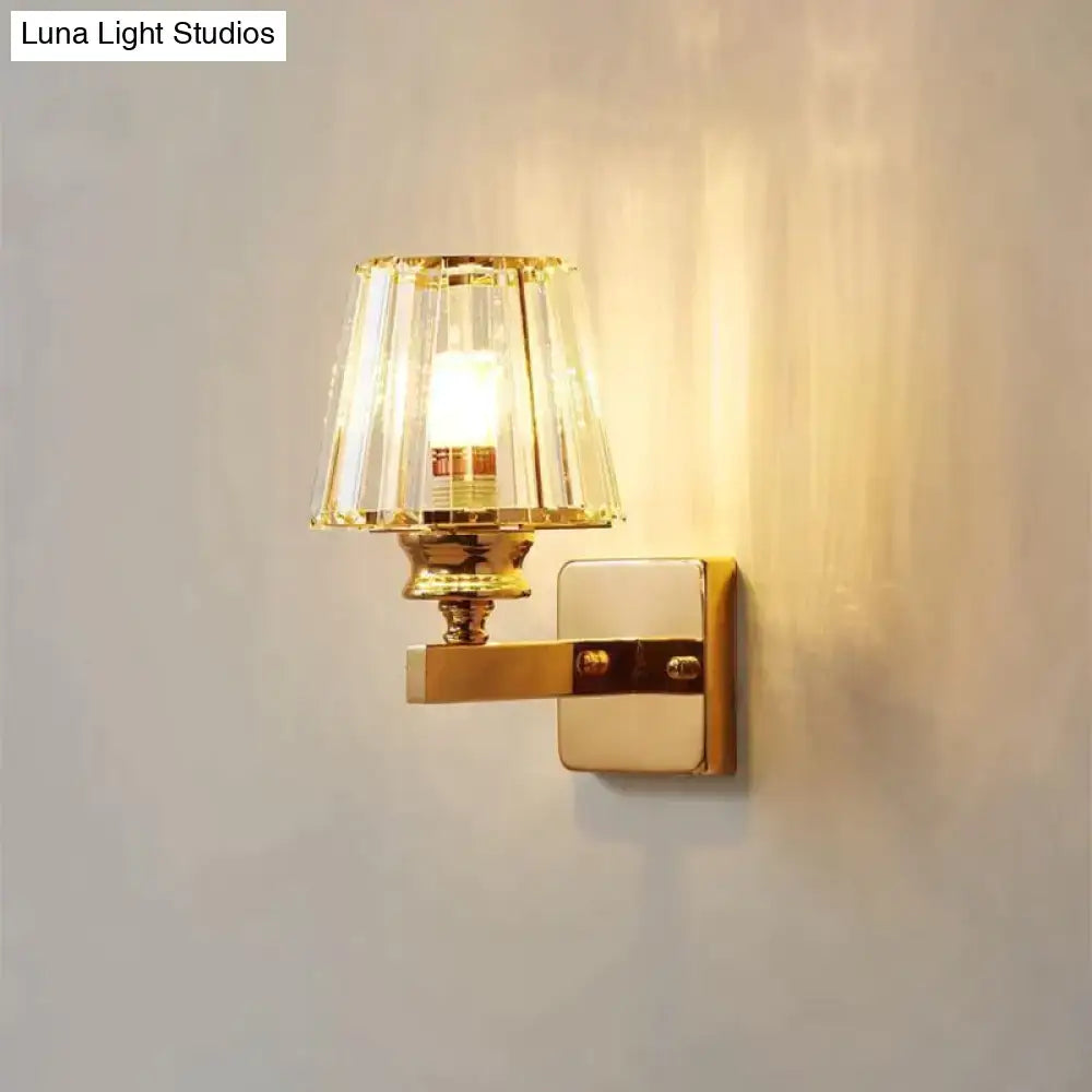 Modern minimalist wall sconce in gold tone with faceted crystal shade and polished brass finish for bedroom lighting