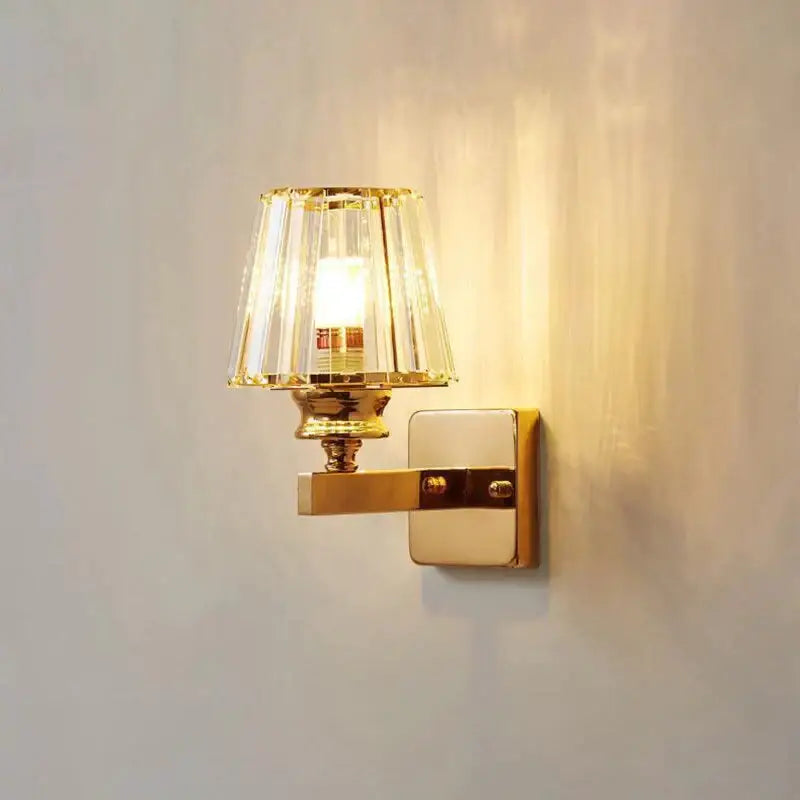 Modern minimalist wall lamp with gold-toned polished brass finish and faceted crystal shade for bedroom lighting
