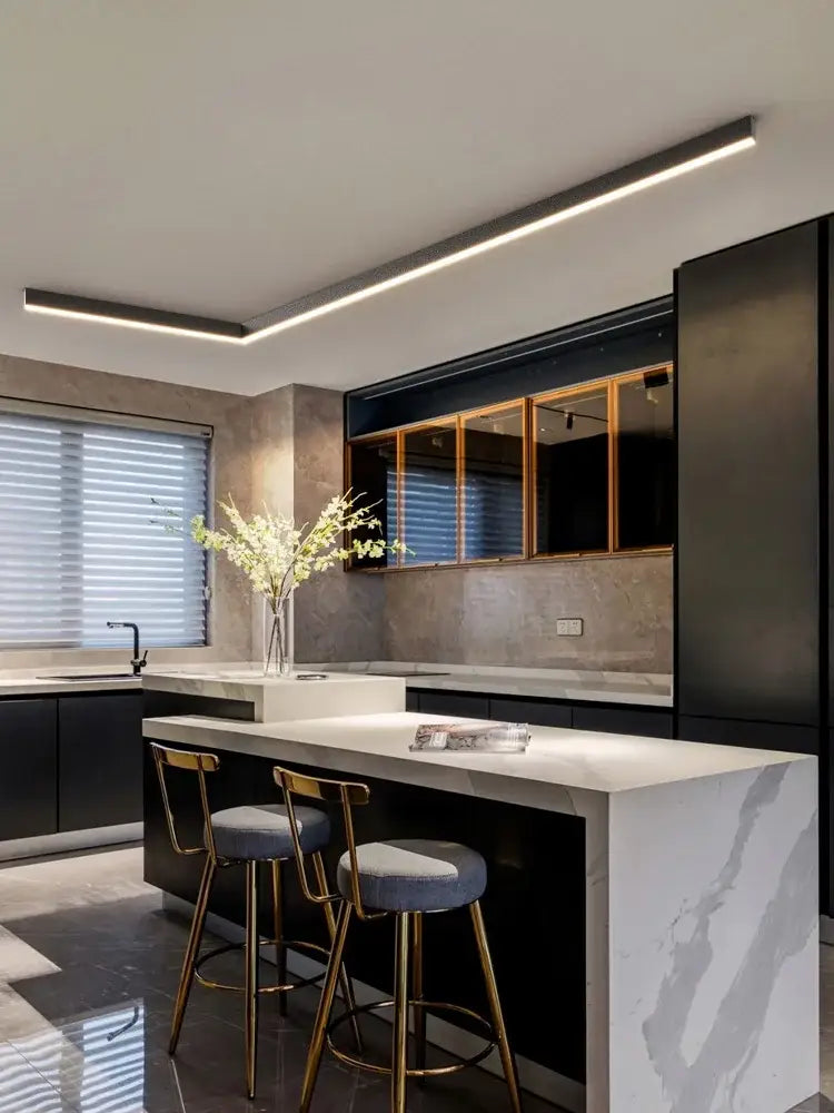 Modern minimalist linear led ceiling light above white marble kitchen island with black cabinetry and gold-toned bar stools decorbites led ceiling