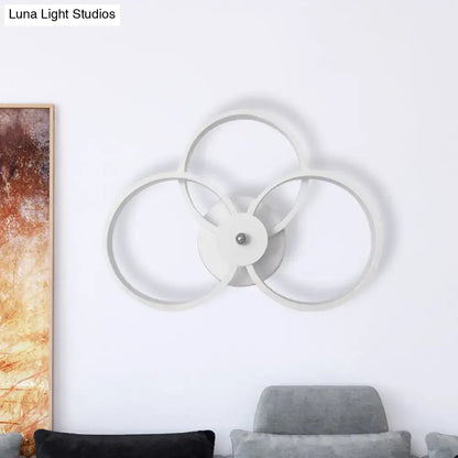 Modern minimalist white wall sconce light with three interlocking rings and central metallic accent for bedroom use