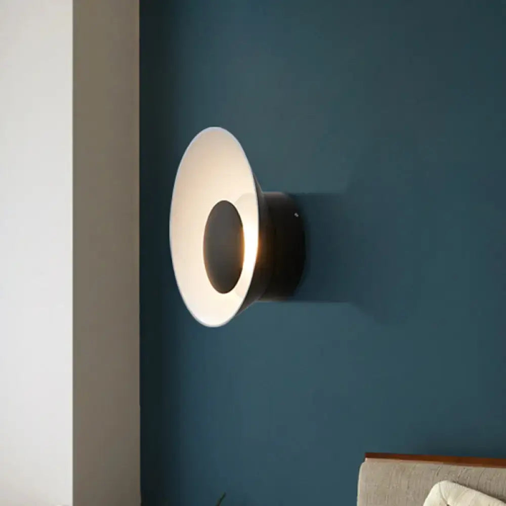 Modern minimalist white and black wall lamp with a sleek circular shade and dark metal base emitting warm light