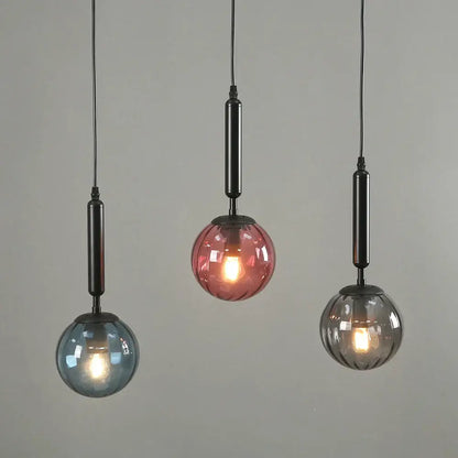 Three modern glass pendant lights in blue pink and gray with painted iron rods for dining room illumination