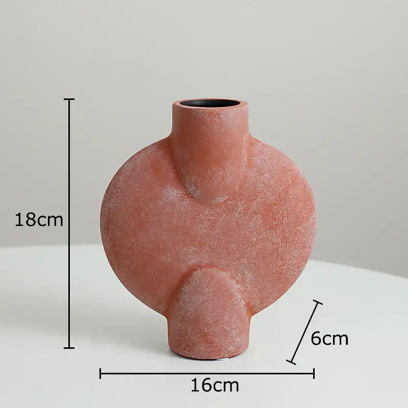 A terracotta-colored decorbites ceramic disc vase with a textured matte finish and modern asymmetrical design