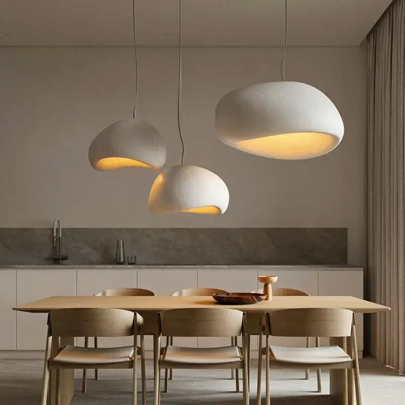 Three off-white handmade led pendant lamps with organic cloud shapes hang above a dining table decorbites chandelier