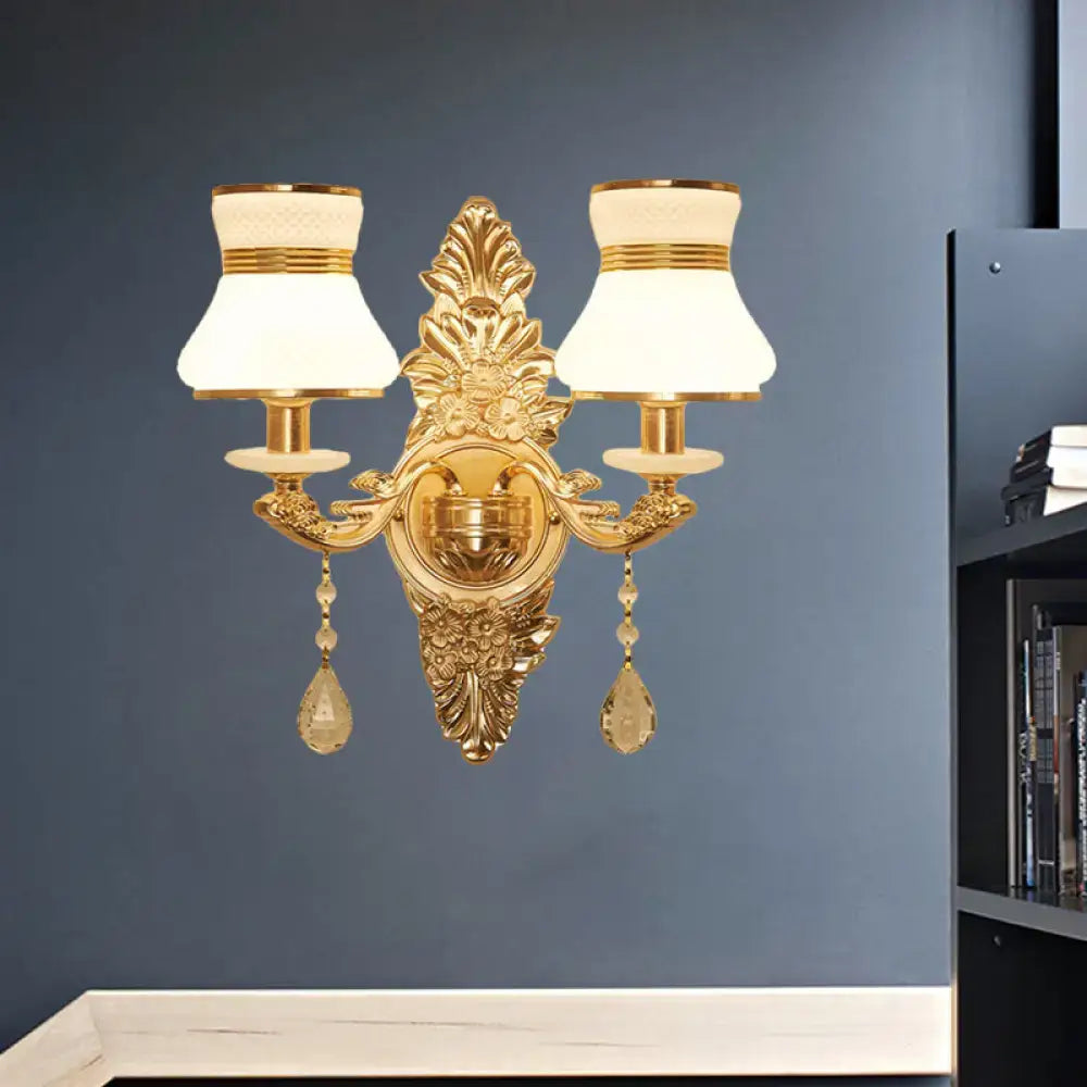 Modern ornate gold wall light with two frosted glass shade lamps and crystal teardrop pendants for bedroom use