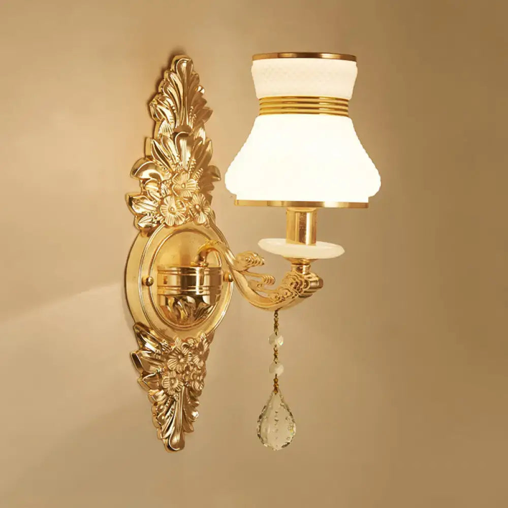 Modern ornate gold wall light with frosted glass shade and crystal teardrop designed as a bedroom sconce