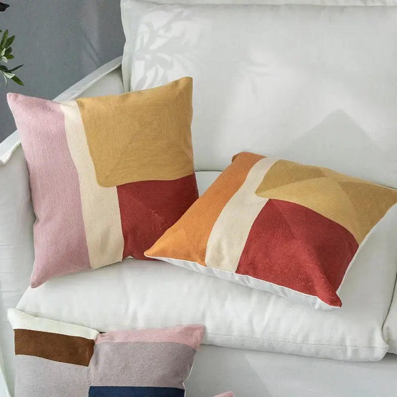 Two square cushion covers with a decorbites geometric cushion pastel patchwork design in pink mustard and terracotta red