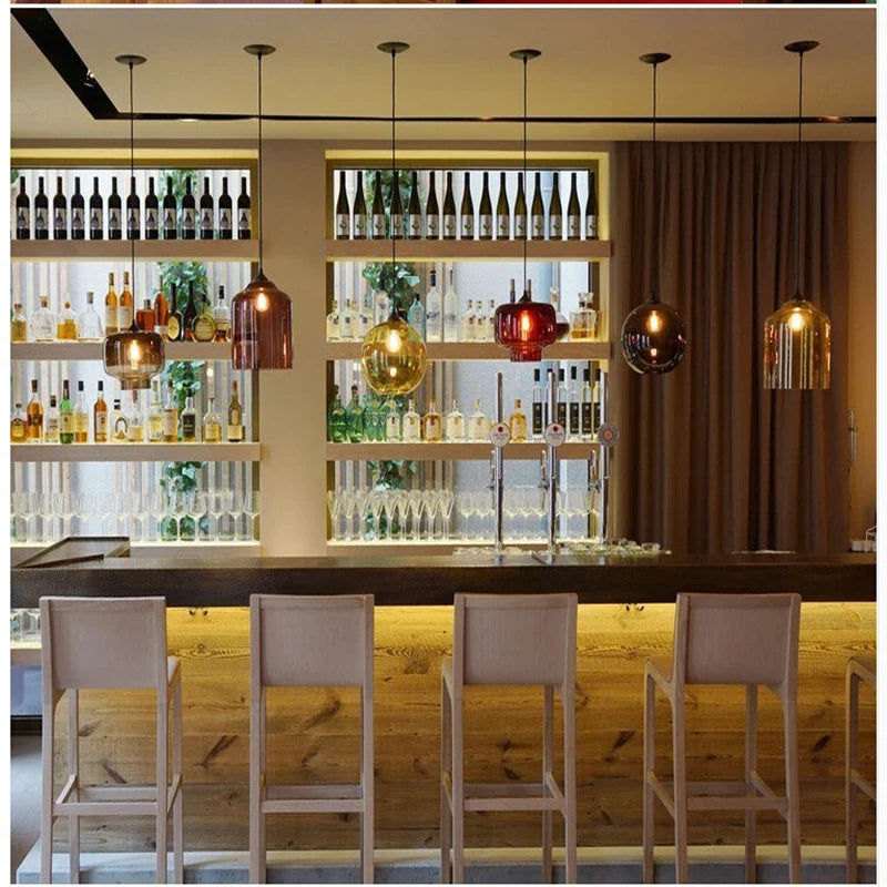 Modern pendant lights with multicolored amber gold and red glass shades hanging above a bar for vintage decor