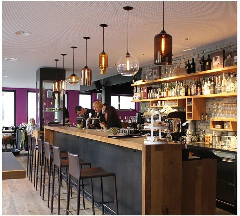 Warm amber and clear glass modern pendant lights hang above a bar in a vintage multicolored loft setting