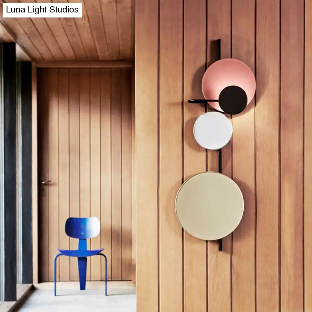 Modern wall-mounted light fixture featuring three stacked circular shades in blush pink, white, and beige with a sleek black metal frame.
