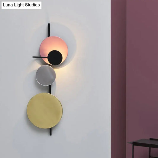 Modern wall light with three stacked circular matte pink silver and gold shades on black metal frame for white yellow bedroom lighting