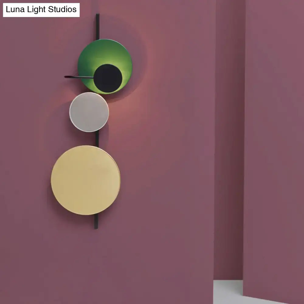 Modern wall light featuring three stacked circular shades in green white and gold on a black rod for white yellow lighting