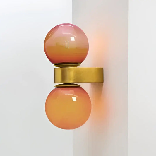 A modern wall lamp with two gradient pink to orange decorbites glass ball led spheres on a polished brass bracket