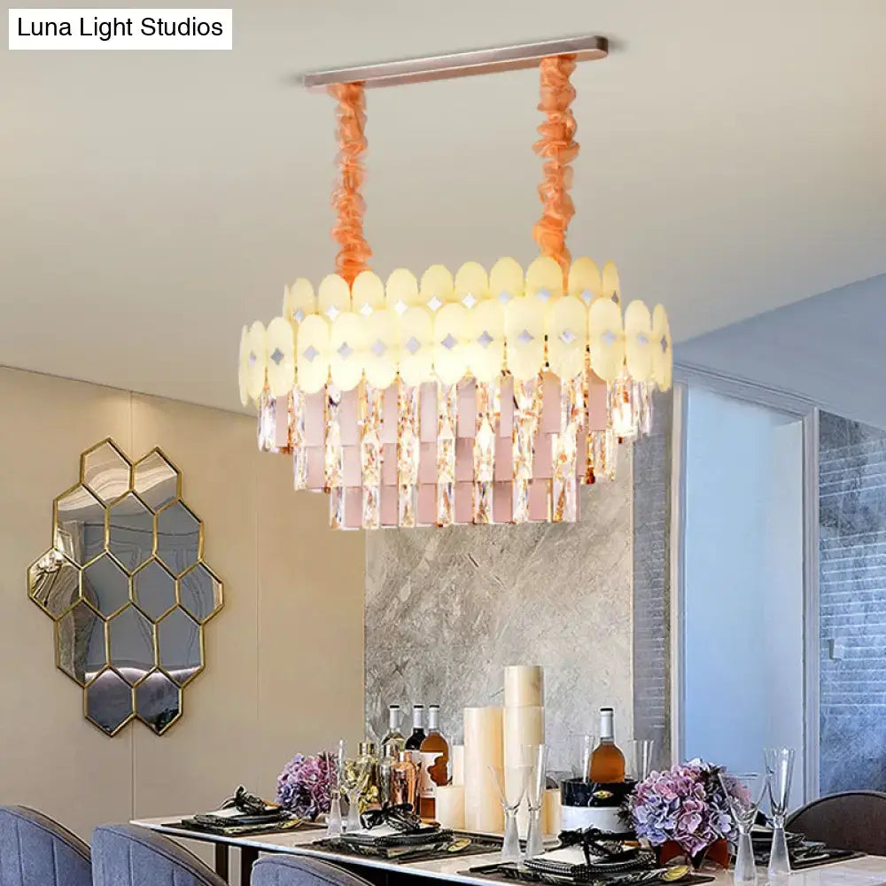 A modern dining room chandelier with clear crystal pink prisms and translucent cream oval plates suspended by peach cords