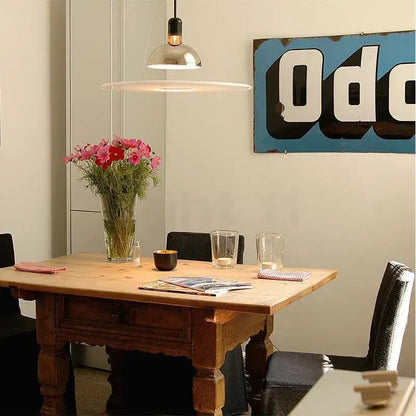 A rustic wooden dining table with a drawer and sturdy legs featuring vibrant pink flowers beneath a decorbites flying saucer chandelier