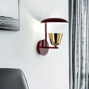 Modern wall light with a matte red dome base and polished gold bell lampshade emitting warm light for bedroom use