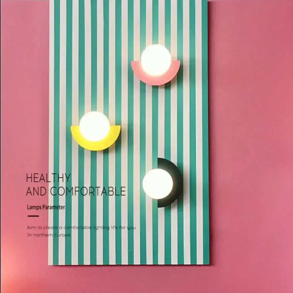 Three modern wall lamps with circular white glass ball led lights and colorful pink yellow and black decorbites glass ball bases