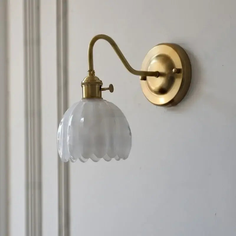 A vintage-style brass wall sconce with a ribbed amber glass shade and a glass copper knob switch for bedroom use