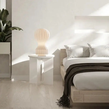 A softly glowing cream-colored silk table lamp with a ribbed ceramic design on a white minimalist side table