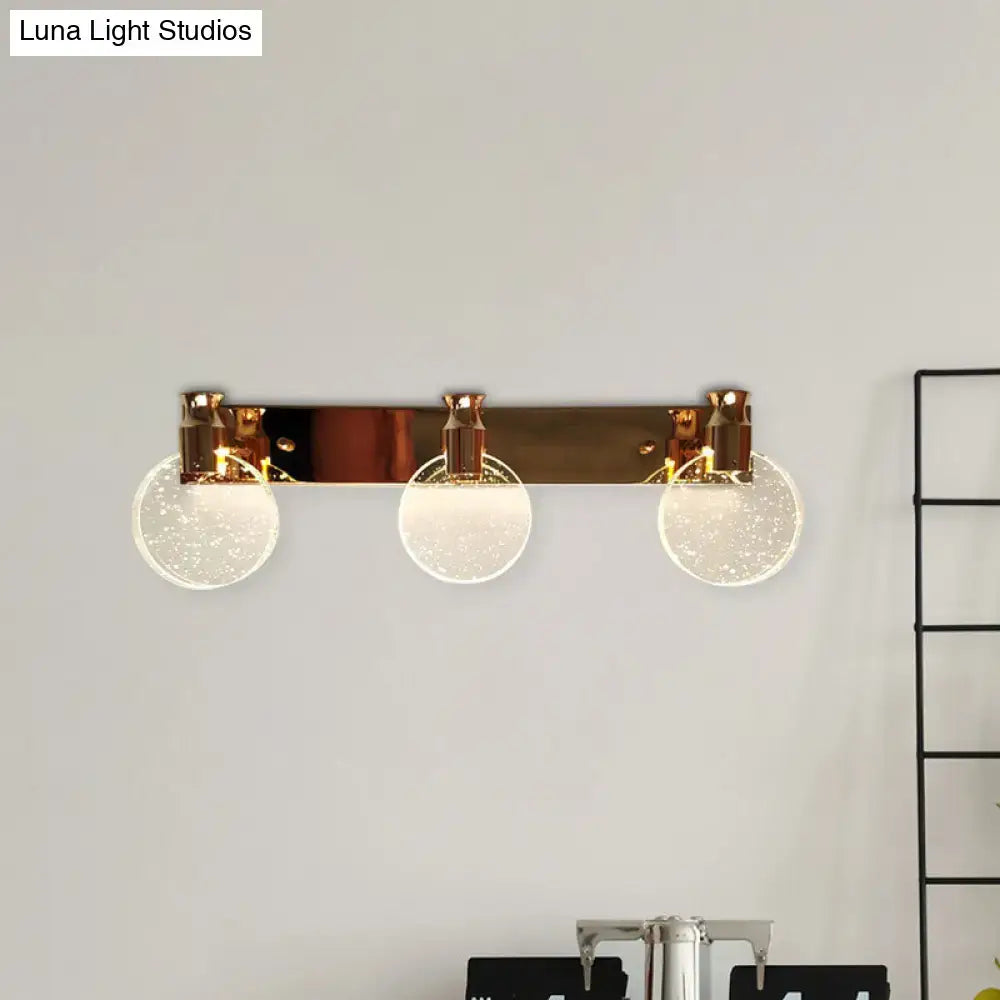 Modern rose gold wall vanity light with three frosted glass globes emitting warm glow for bathroom vanity use